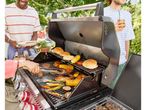 People grilling burgers, chicken, corn, and vegetables on a barbecue in a garden.