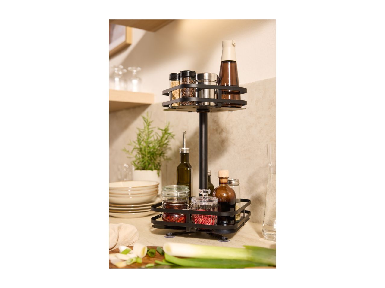 A black two-tier spice rack with various spices and oils on a kitchen counter.