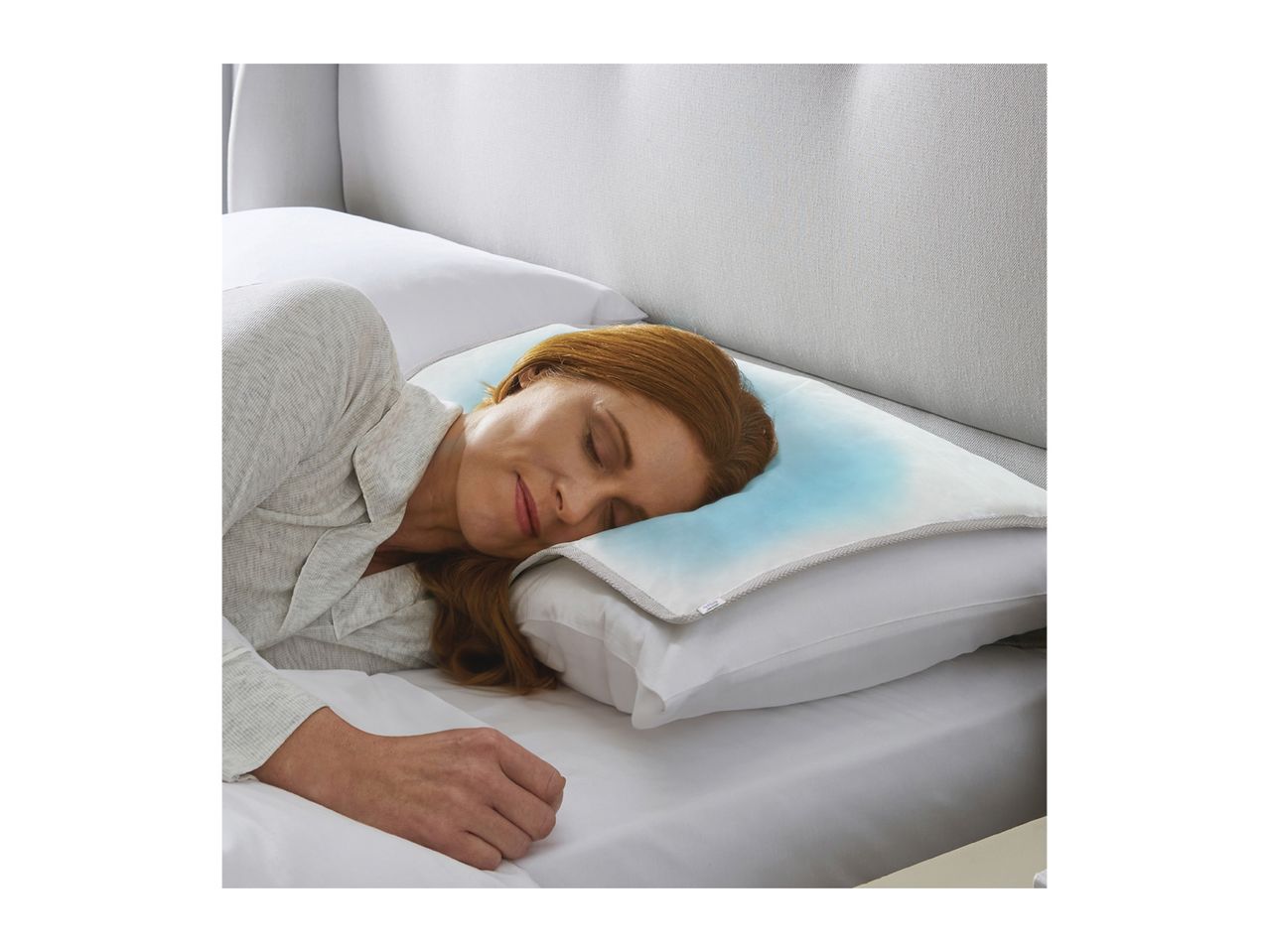 Woman sleeping on a bed with a cooling pillow pad, wearing light grey sleepwear.