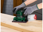 Gloved hands using a PARKSIDE orbital sander on a wooden board.