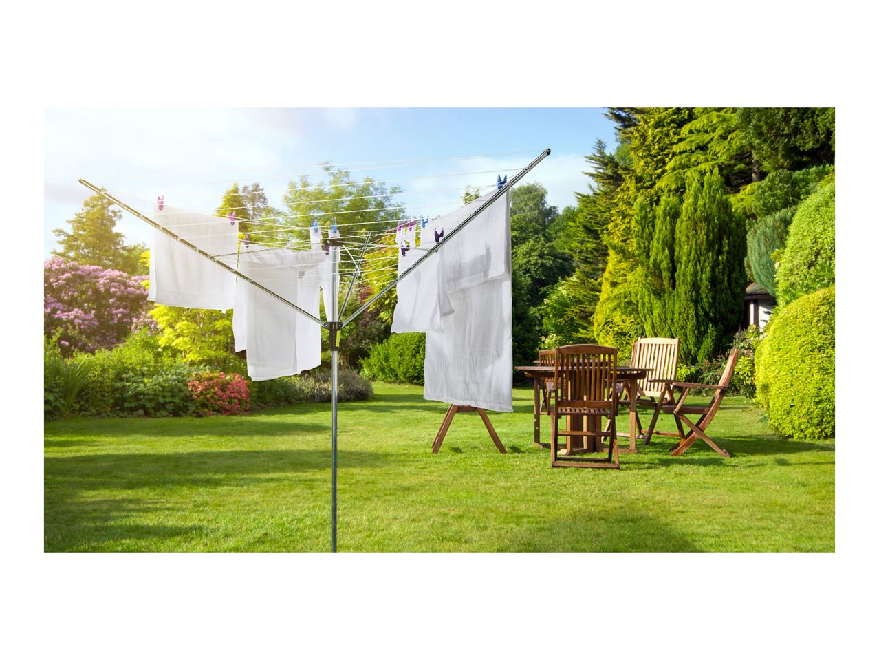 Rotary clothesline with white laundry drying in a sunny garden with wooden patio furniture.