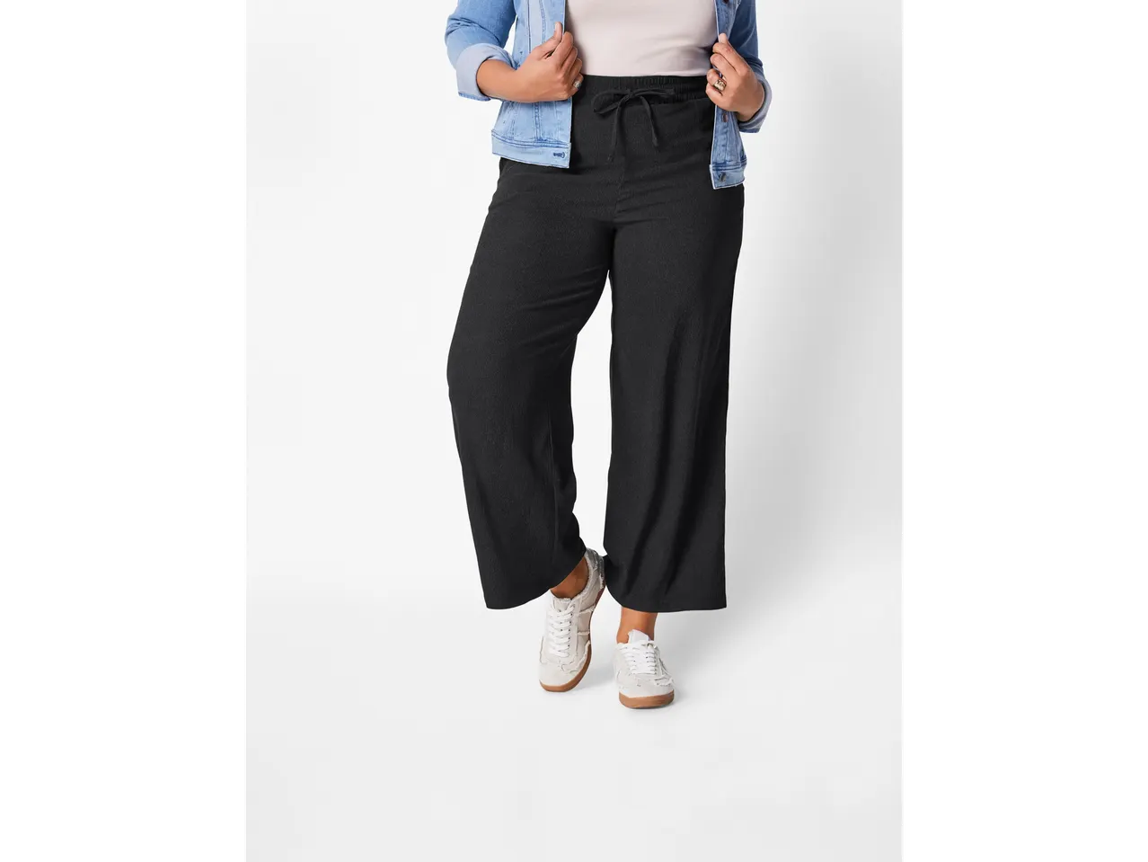 Femeie purtând pantaloni largi negri și adidași deschiși la culoare.
