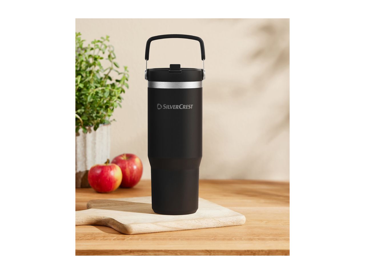 A black Silvercrest travel mug on a wooden board with apples and a plant.