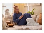Woman in blue loungewear relaxing on a sofa with a tablet and a heated foot warmer.