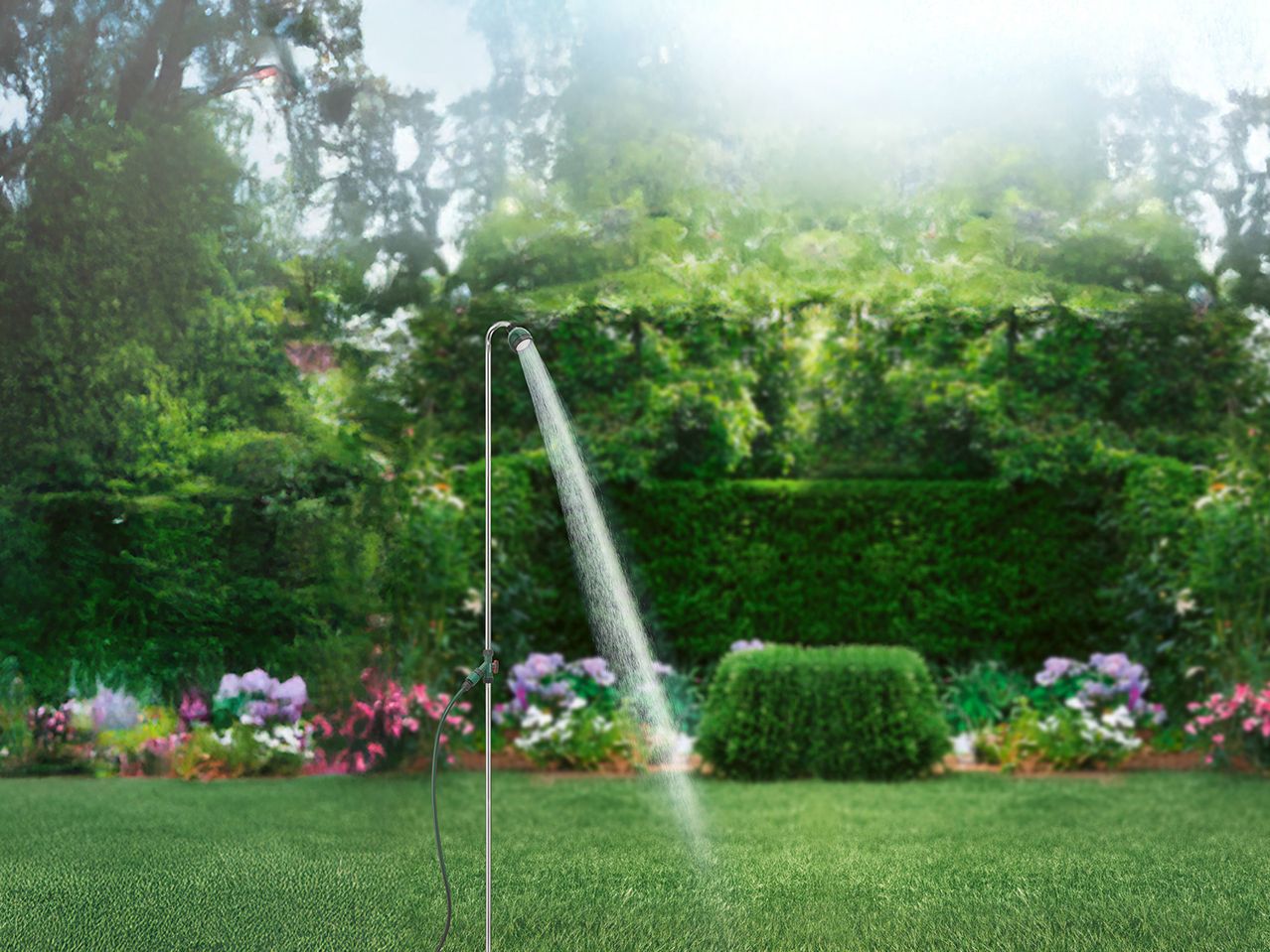 Ένα εξωτερικό ντους Gardena στέκει σε έναν καταπράσινο κήπο, ψεκάζοντας νερό.