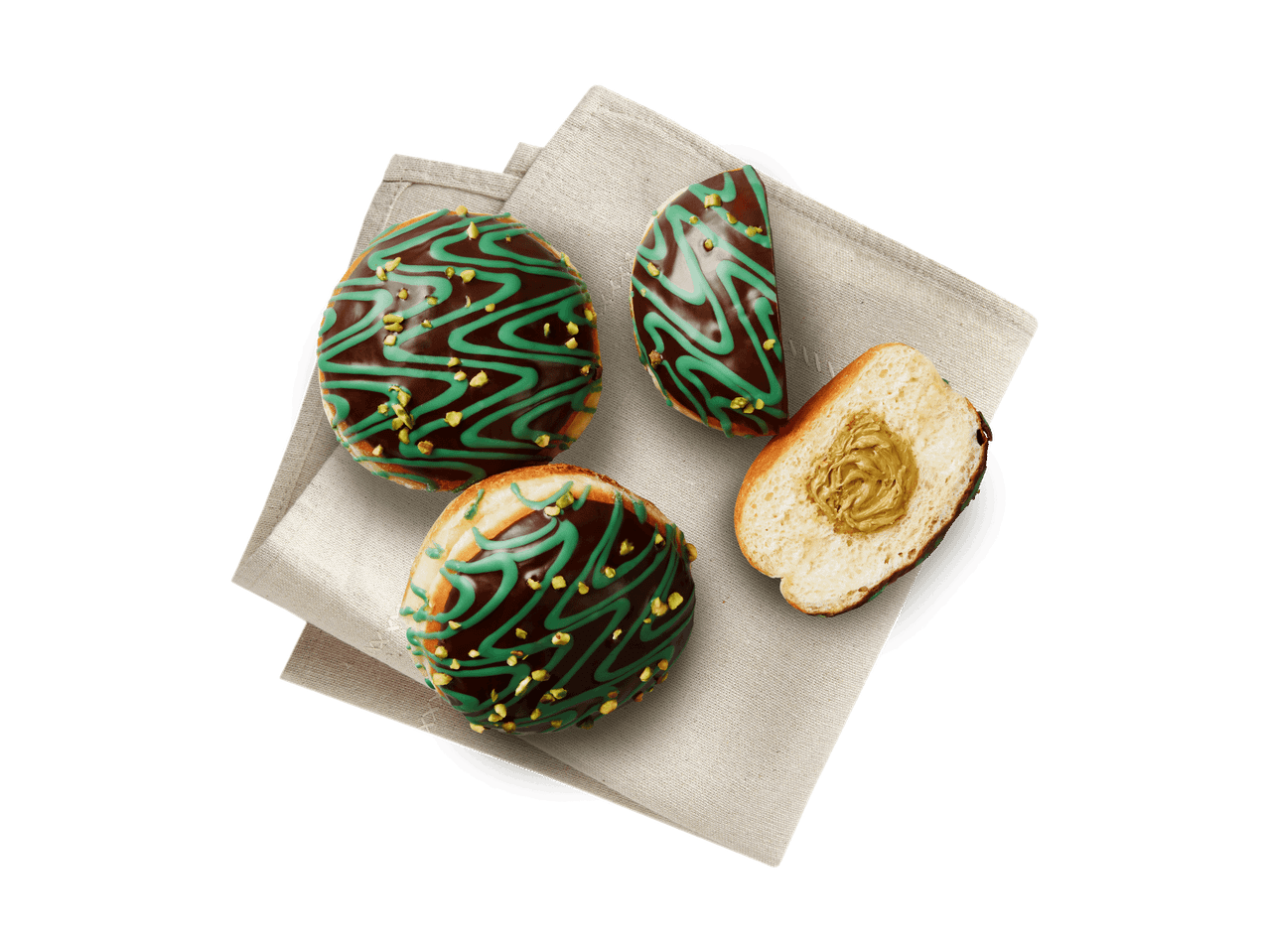 Drei Schoko-Pistazien-Donuts auf einer Serviette, einer davon halbiert mit Pistazienfüllung.