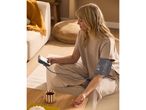 Woman measuring blood pressure at home, with a cup of tea on a wooden table.