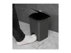 A person's foot in a white sock opening a grey pedal bin with a textured design.