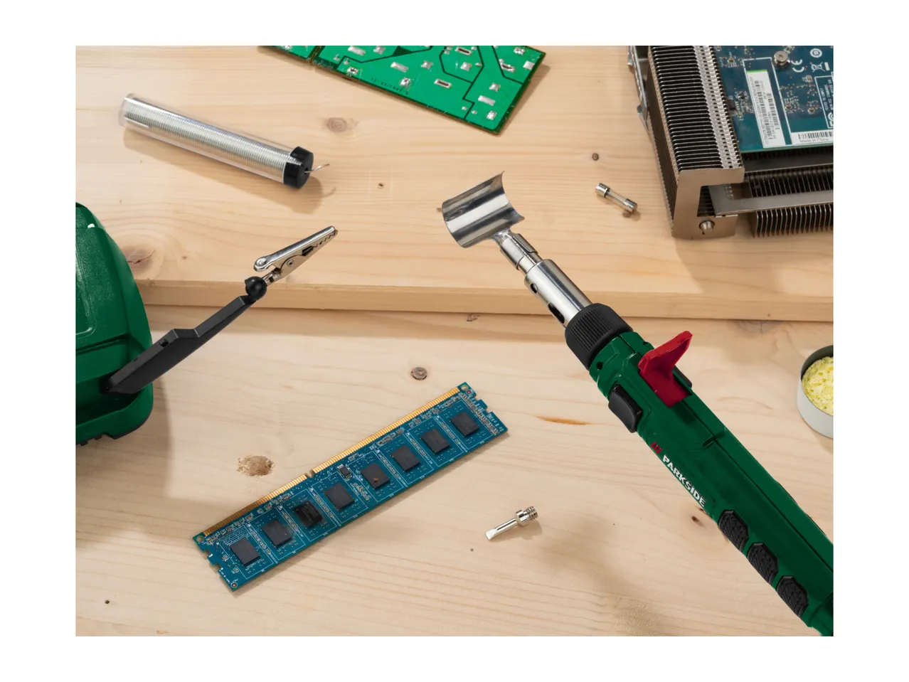 A soldering iron and electronic components like RAM and circuit boards on a wooden surface.
