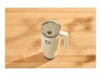 Cream-colored travel mug with a handle and straw on a wooden table.