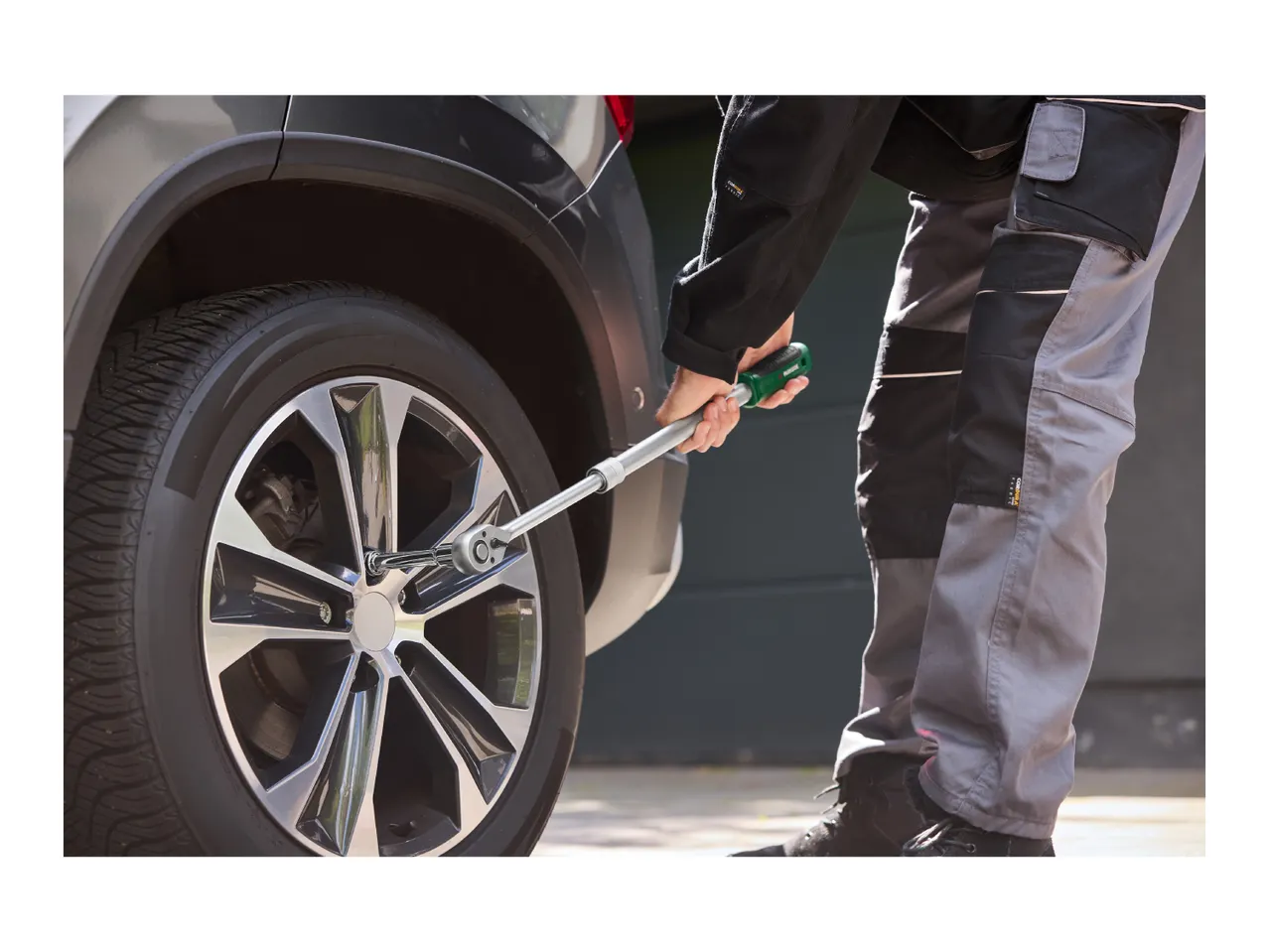 A person using an extendable wheel wrench to loosen a lug nut on a car wheel.