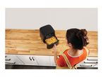 Overhead view of a person pulling out a basket of fries from an air fryer on a kitchen counter.