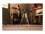 Laser level on a tripod projecting a red line, with a person hanging a wooden rack in the background.
