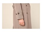 Close-up of a person wearing a beige trench coat with tortoise shell buttons and a gold ring.