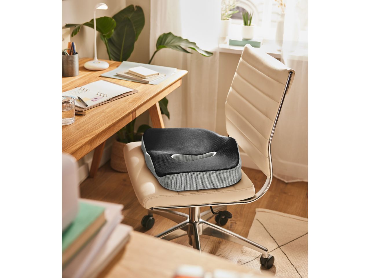 Ergonomic seat cushion on an office chair at a wooden desk with a lamp and plants.