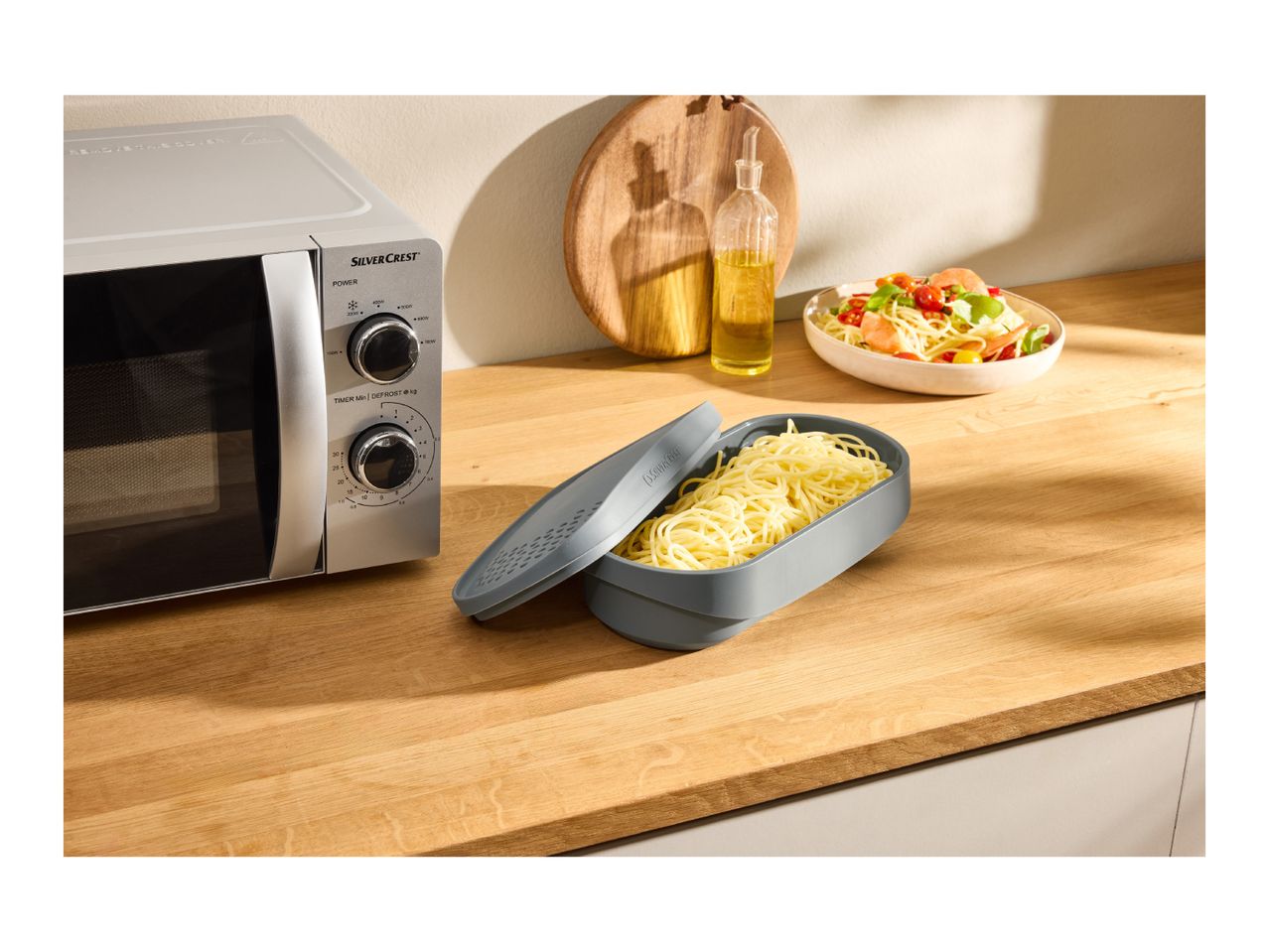 Microwave oven, pasta cooker, and a bowl of pasta salad on a wooden kitchen counter.