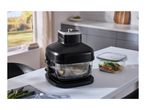 Black air fryer on a kitchen counter with cooked food inside and fresh asparagus nearby.