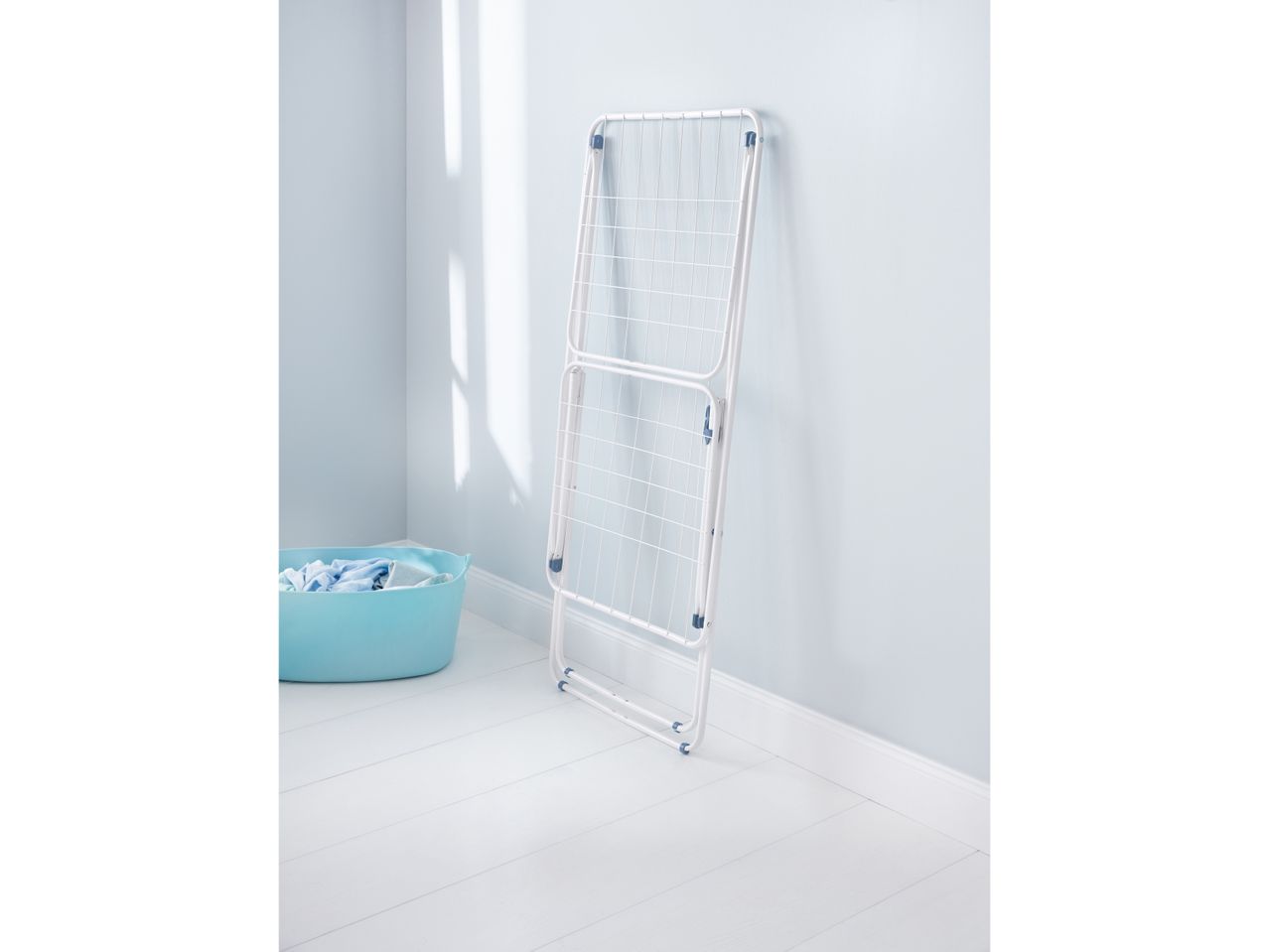 A white foldable laundry drying rack stands against a light blue wall, next to a light blue laundry basket.