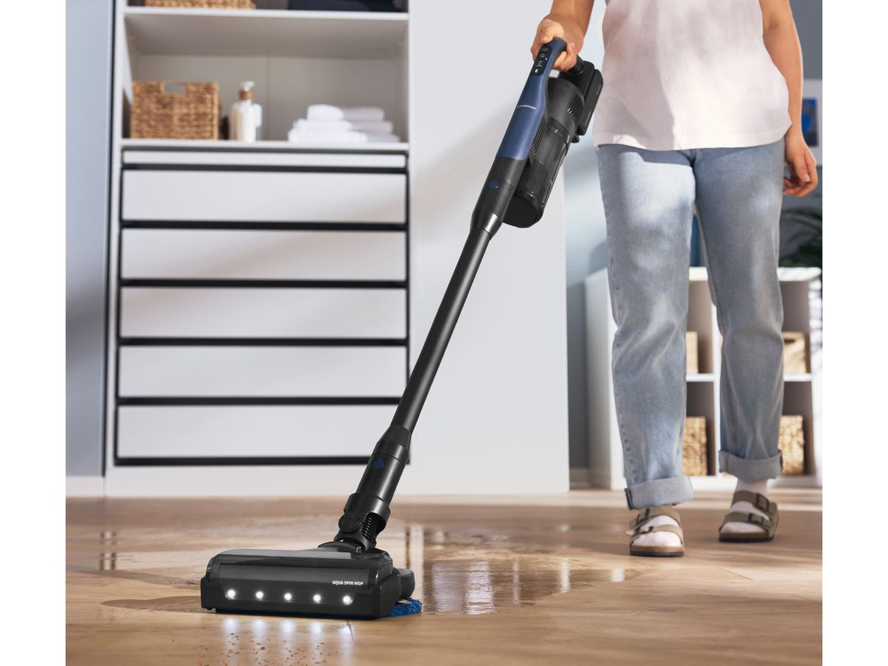 Person cleaning a wooden floor with a cordless wet and dry vacuum cleaner.