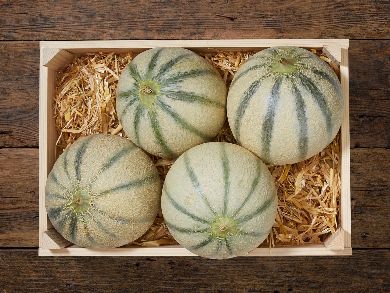 Vier Melonen in einer Holzkiste.