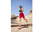 Woman running in red cycling shorts and black sports bra on a sunny day.