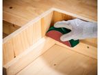 Hand in a glove sanding the inside corner of a wooden box with a sanding block