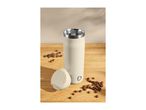 Cream-colored travel mug with lid and coffee beans on a wooden surface.