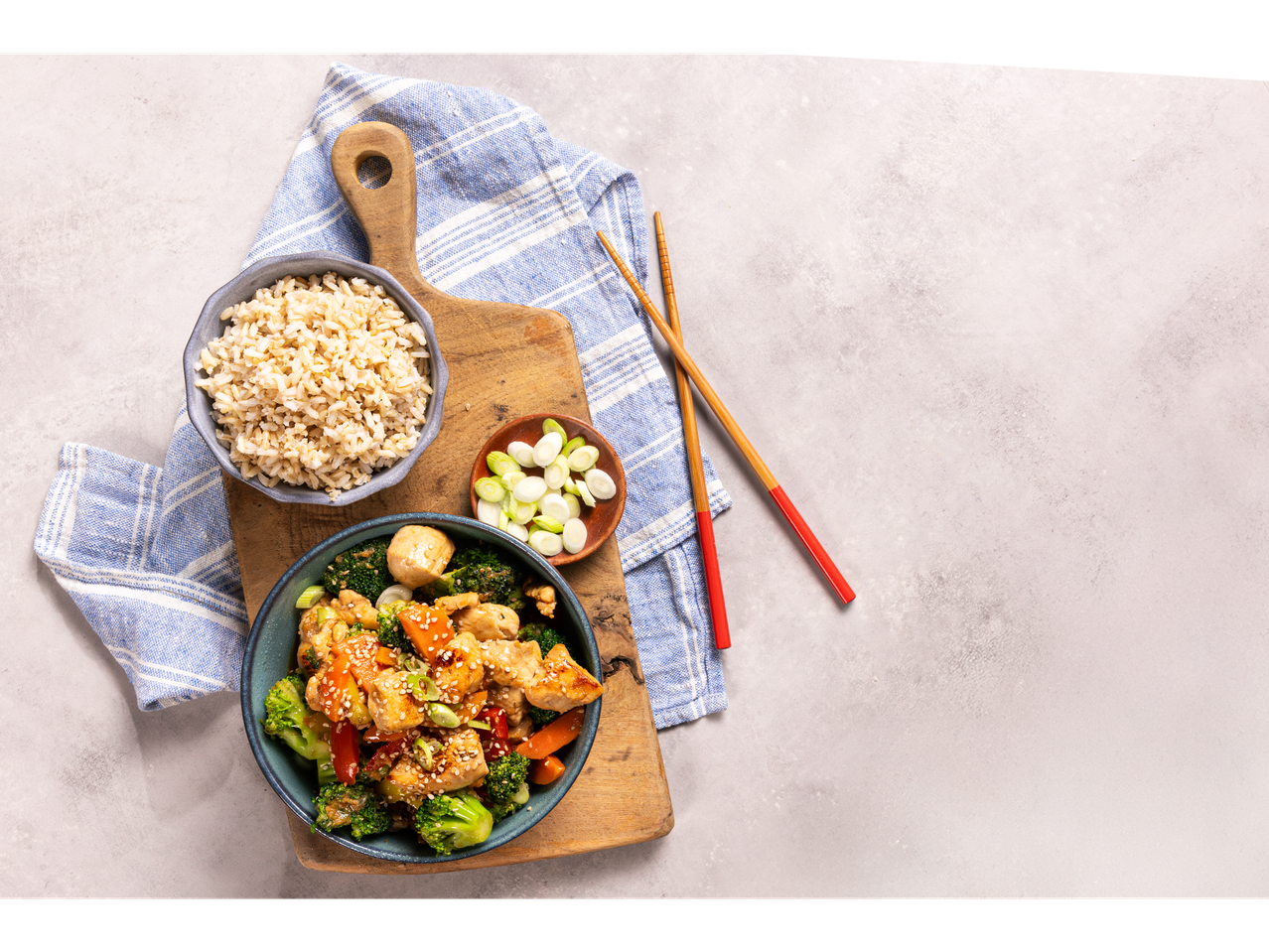 Ginger stir-fry with chicken, broccoli, carrots, and brown rice, served with chopsticks.