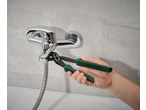 Hand using pliers to tighten a chrome shower mixer tap with a hose in a bathroom.