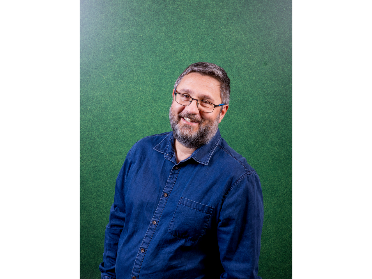 A smiling man in a blue denim shirt against a green background.