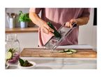 Person slicing zucchini with a mandoline slicer onto a wooden cutting board in a kitchen.
