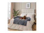 A cocker spaniel dog lies on a grey fluffy dog bed on a bed with beige bedding in a bedroom.