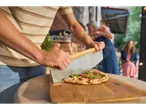 Wood-fired pizza being sliced with a pizza cutter on a wooden board.