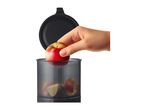 A hand placing a whole apple into a food processor with chopped apples inside.