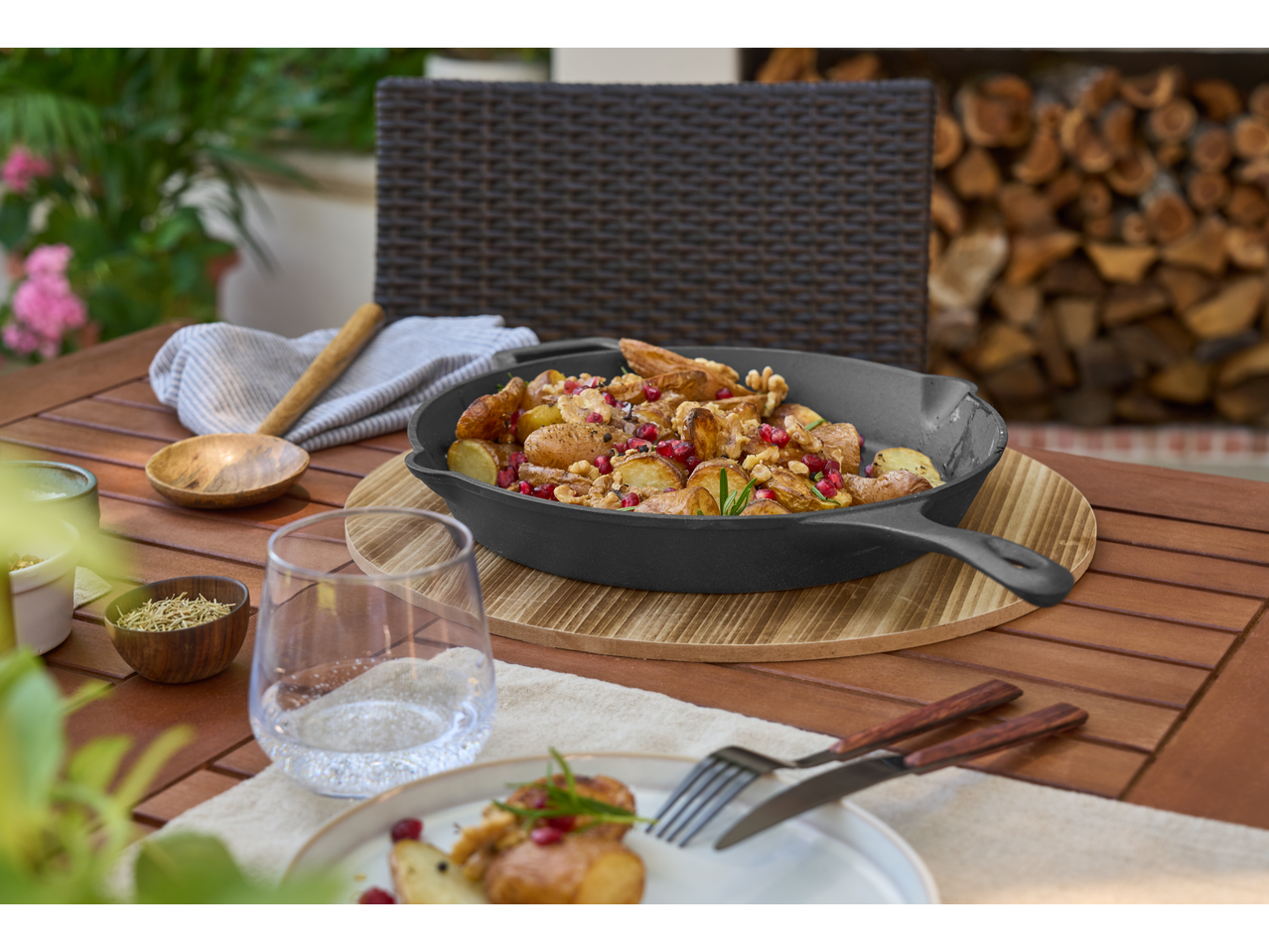 Tigaie din fontă cu cartofi prăjiți, rodie și nuci pe o masă de lemn.