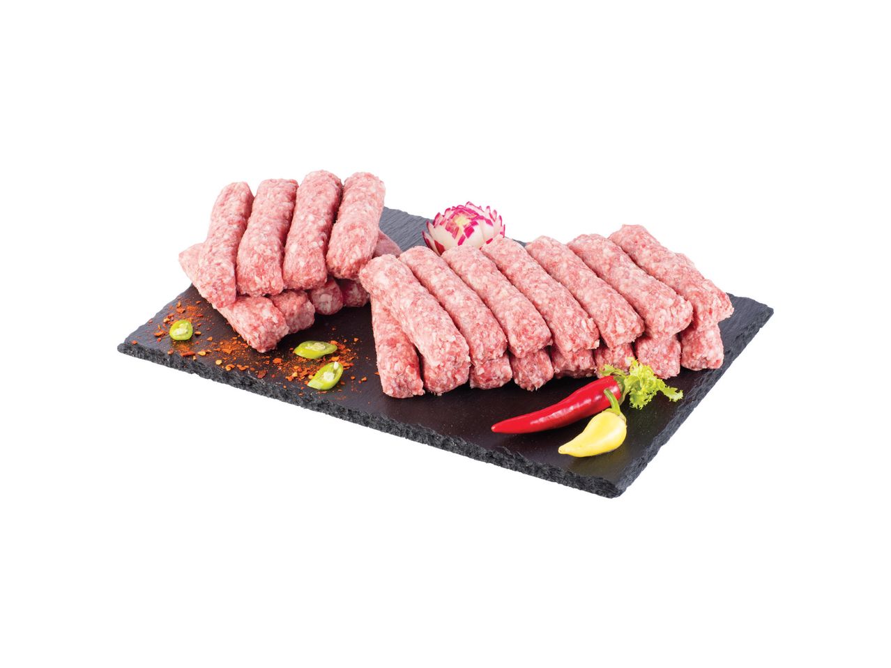 Sveži ćevapi na crnoj ploči sa začinima i papričicama.