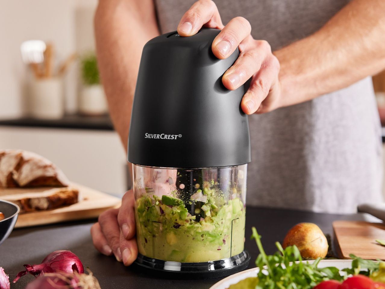 A person using a SilverCrest food chopper to prepare avocado and red onion.