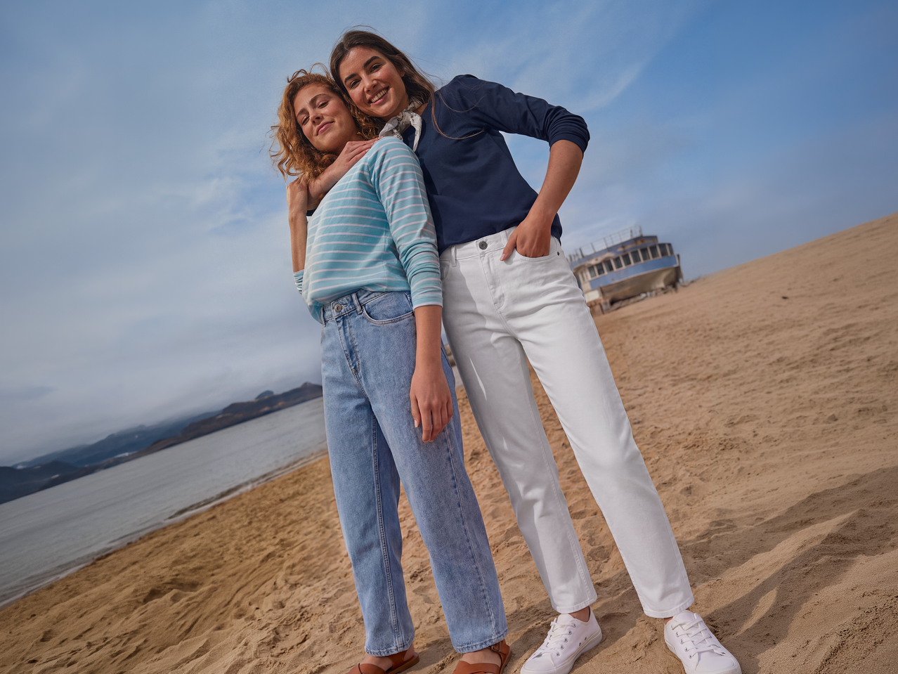 Δύο γυναίκες με casual μακρυμάνικες μπλούζες και τζιν σε αμμώδη παραλία.