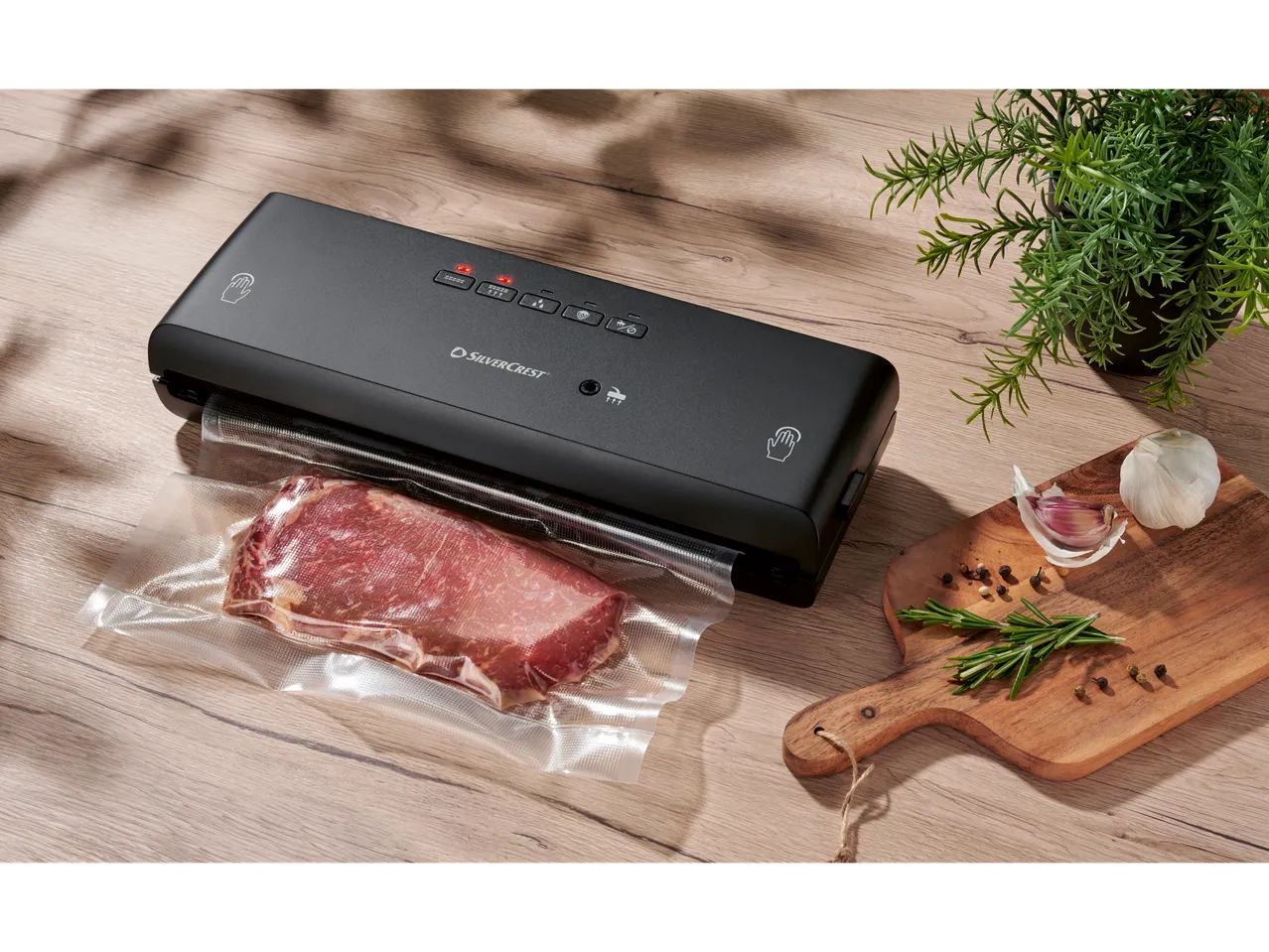 SILVERCREST® Vacuum Sealer with vacuum-sealed meat, rosemary, garlic, and peppercorns on a wooden board.