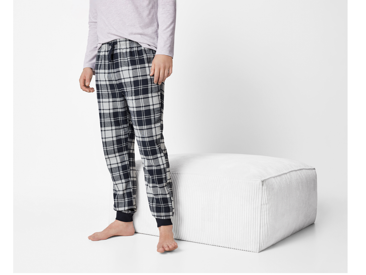 Pantaloni de pijama din flanelă Esmara Men, în carouri, cu manșete elastice, lângă un otoman alb.