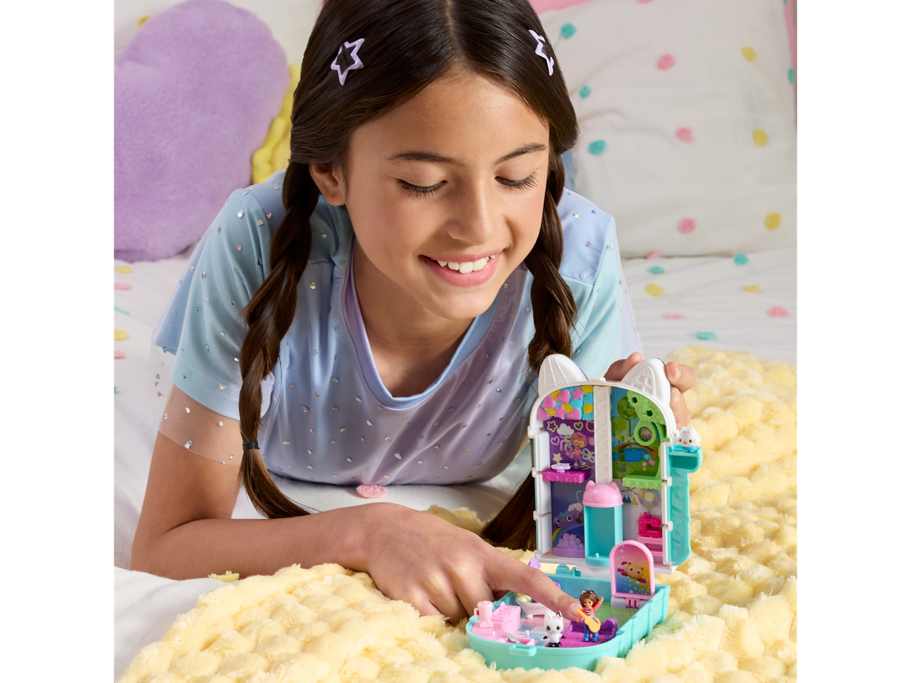 A girl playing with a Gabby's Dollhouse Purrfect Playset on a fluffy blanket.