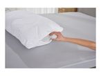A hand adjusting the filling of a white quilted pillow with a zipper on a grey bed.