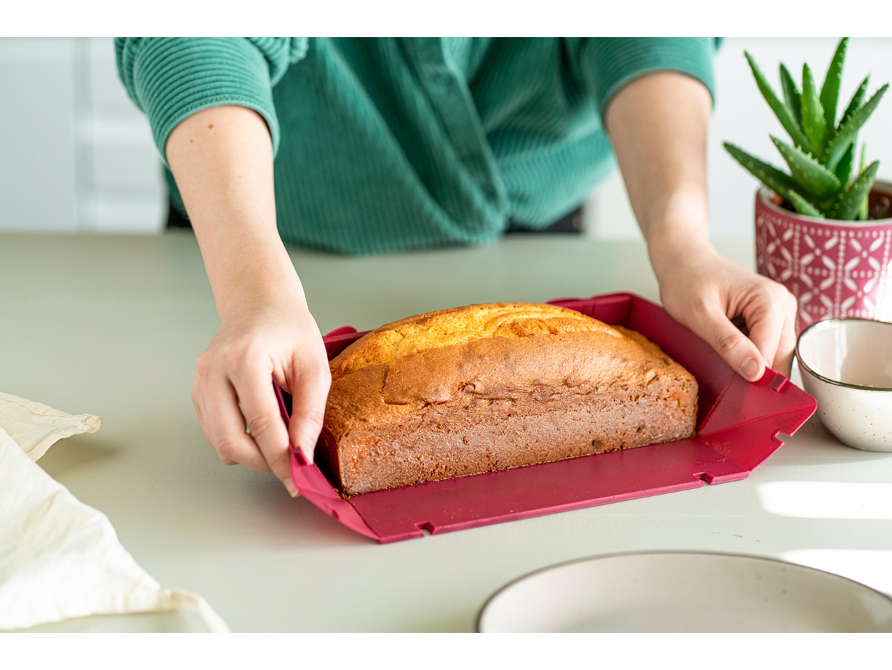 Hände entnehmen einen goldbraunen Kuchen aus einer roten Coox Wunderform® Springform.