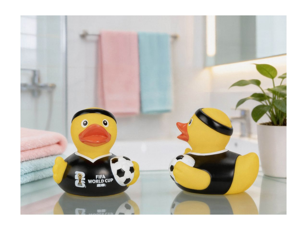 Two rubber ducks in black jerseys with a football, in a bathroom setting.