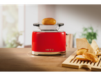 Red toaster with a bun on top, next to a wooden board with bread rolls.