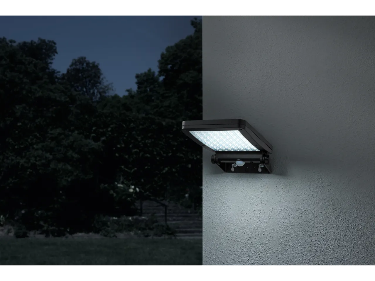 Lampă solară cu senzor de mișcare, montată pe perete, iluminând o zonă exterioară întunecată.