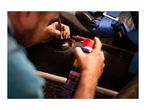 A person's hands applying lubricant to a car part with a spray can.