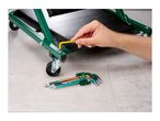 Person assembling a green workshop creeper with a yellow hex key, with a set of hex keys nearby.