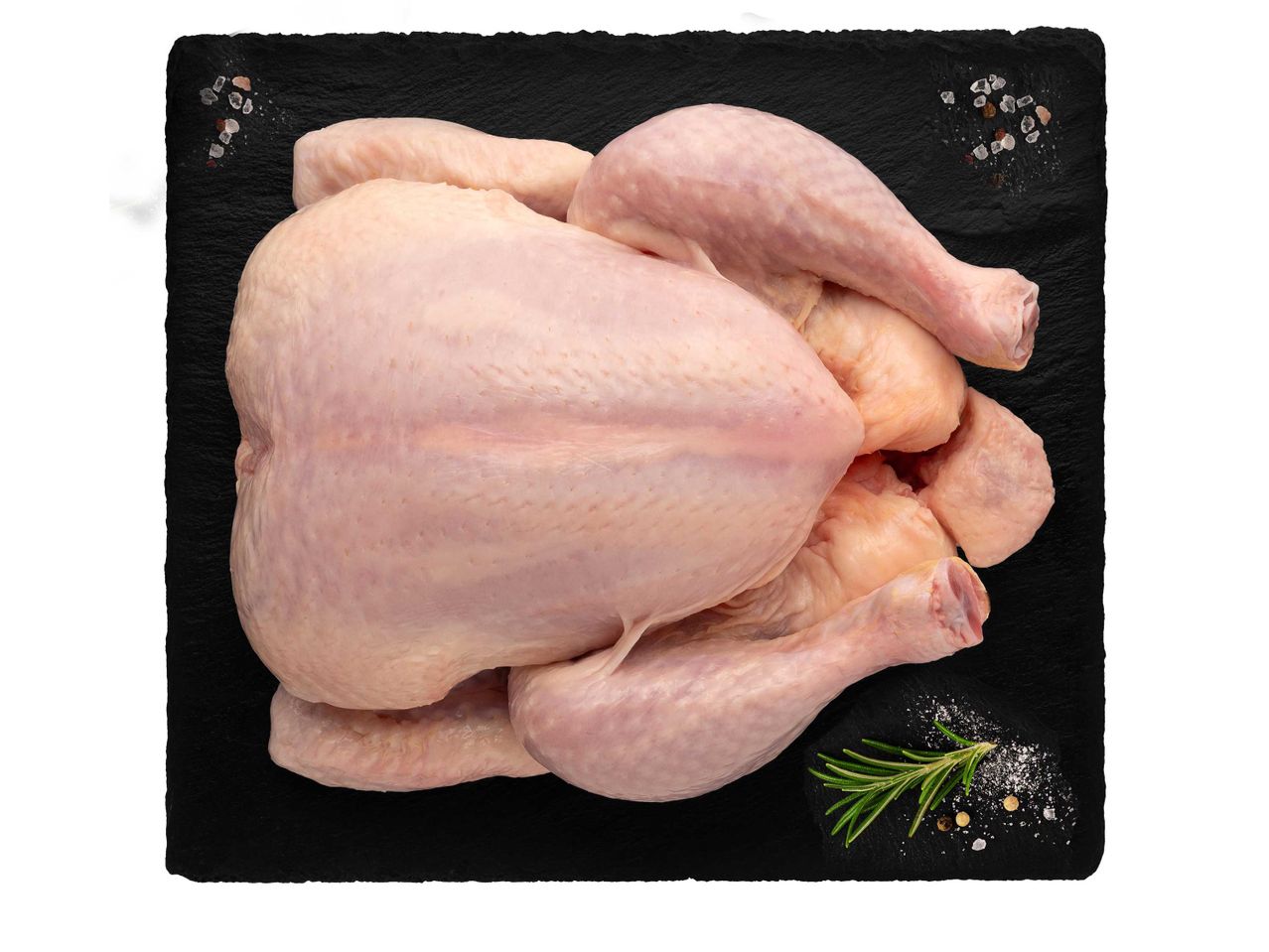 Nyers egész csirke fekete palatáblán, rozmaringgal és fűszerekkel