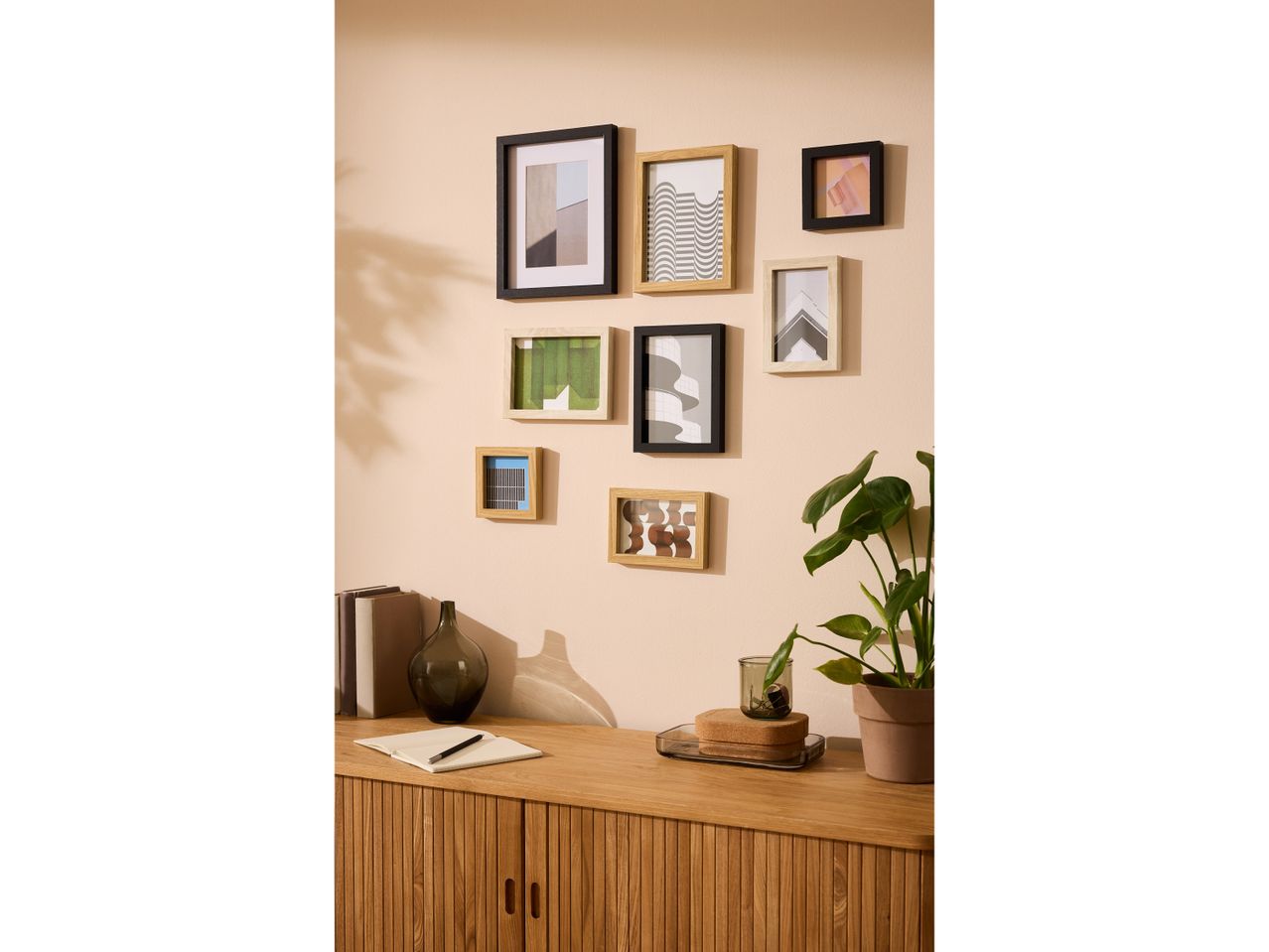 Una credenza in legno con ante a doghe, sormontata da libri, un vaso e piante, con quadri appesi alla parete.